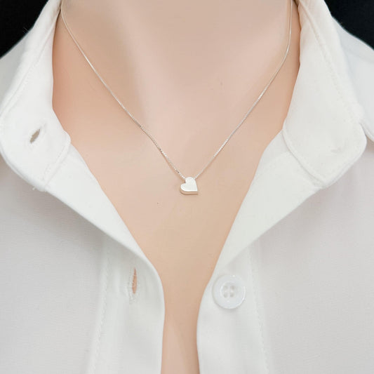 A delicate silver heart-shaped pendant necklace is worn around the neck of a person wearing a white collared shirt.
