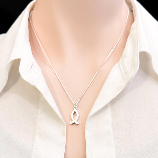 A silver necklace with a pendant is worn around a person's neck.