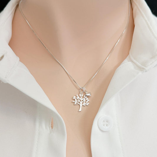 A silver necklace with a tree pendant is worn around a person's neck, and a white collared shirt is visible underneath.