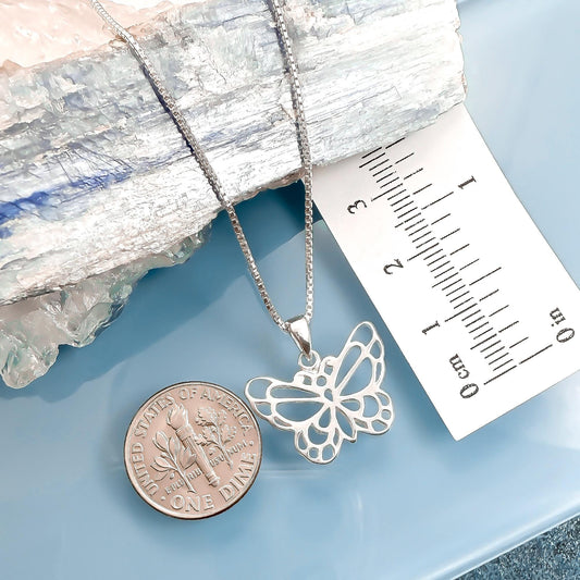 a silver butterfly pendant on a chain, placed next to a US quarter coin for scale.