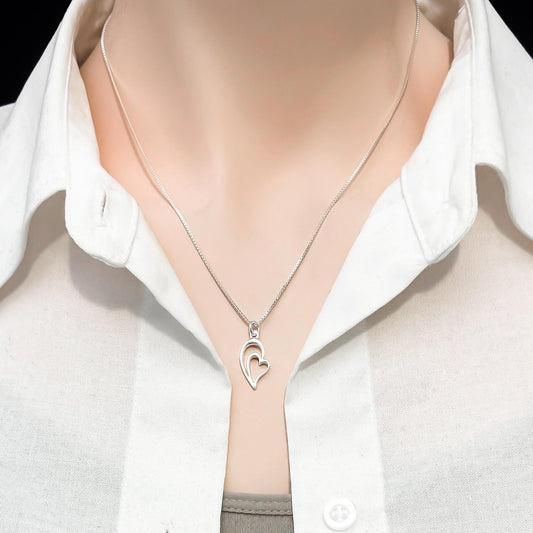 A silver necklace with a heart-shaped pendant is worn around a person's neck, who is wearing a white collared shirt.