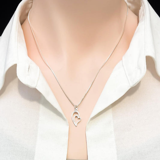 A silver necklace with a heart-shaped pendant is displayed on a mannequin's neck.
