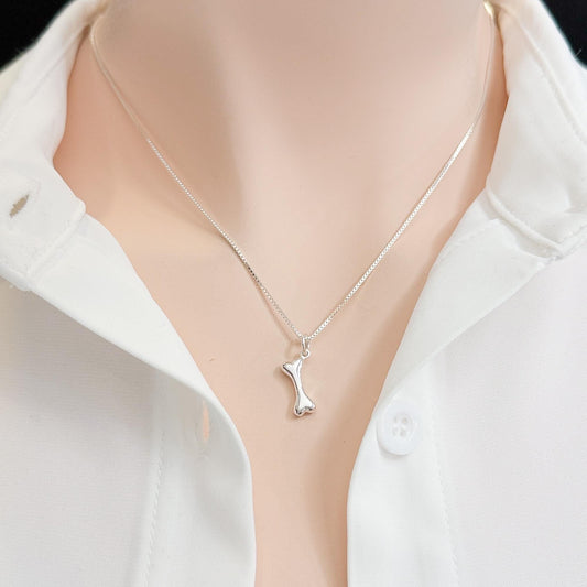 A silver necklace with a pendant is displayed on a person wearing a white collared shirt.