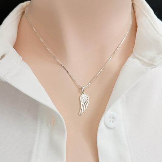 A silver necklace with a pendant featuring a wing design is shown on a person wearing a white collared shirt.