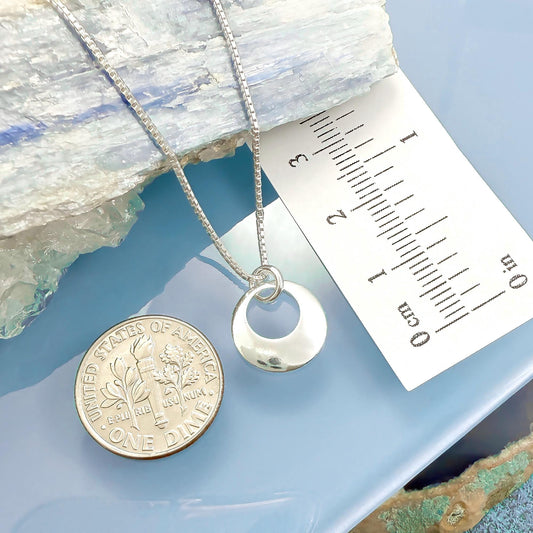 a silver necklace with a pendant, a silver coin, and a ruler on a blue surface.