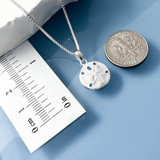 A silver necklace with a pendant is placed next to a U.S. one dollar coin on a blue surface.