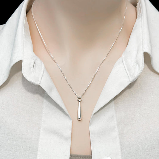 A close-up view of a silver necklace with a pendant, worn around a person's neck.