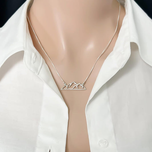 A silver necklace with a pendant in the shape of a mountain on a chain.