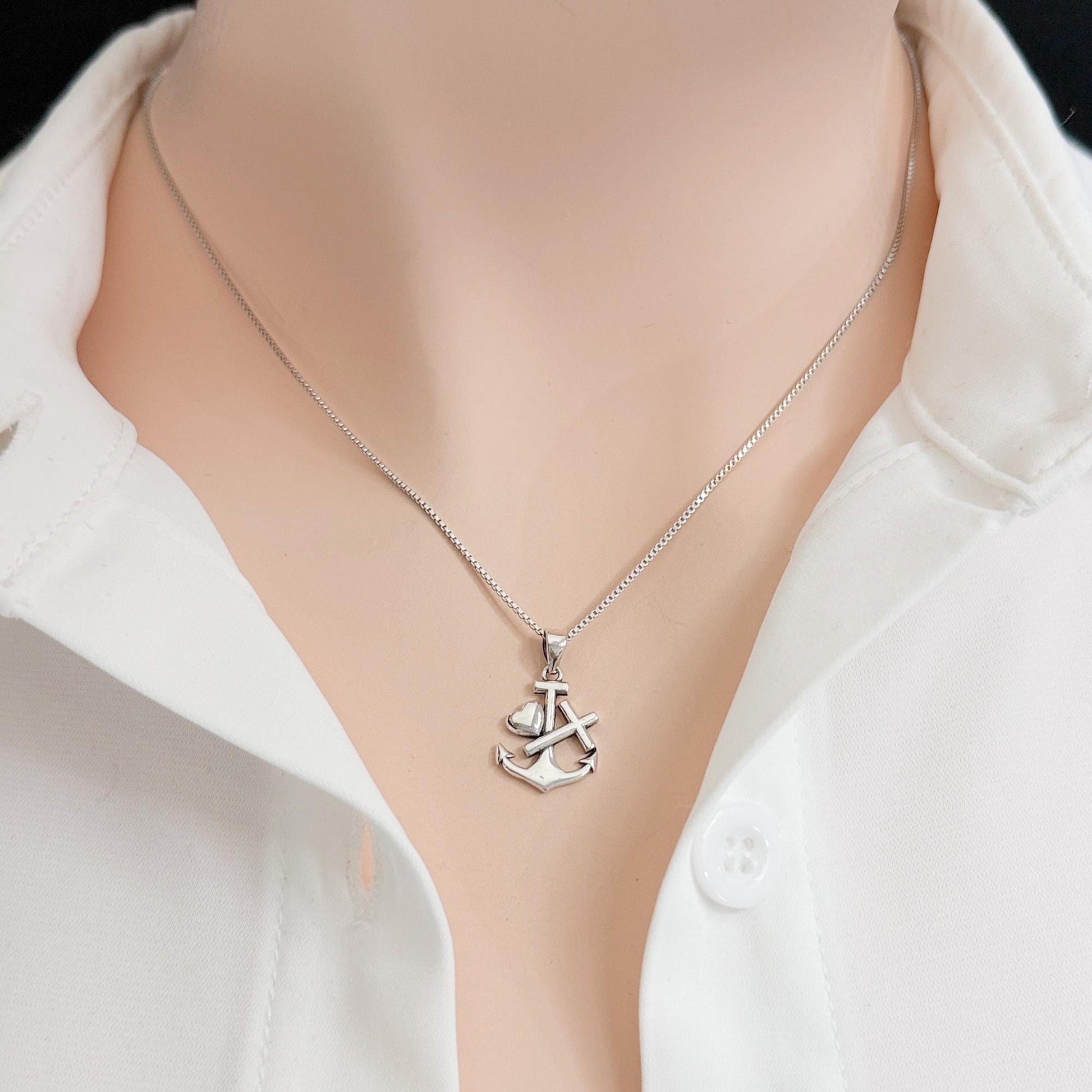 A silver necklace with a pendant featuring an anchor design is shown against a white shirt.