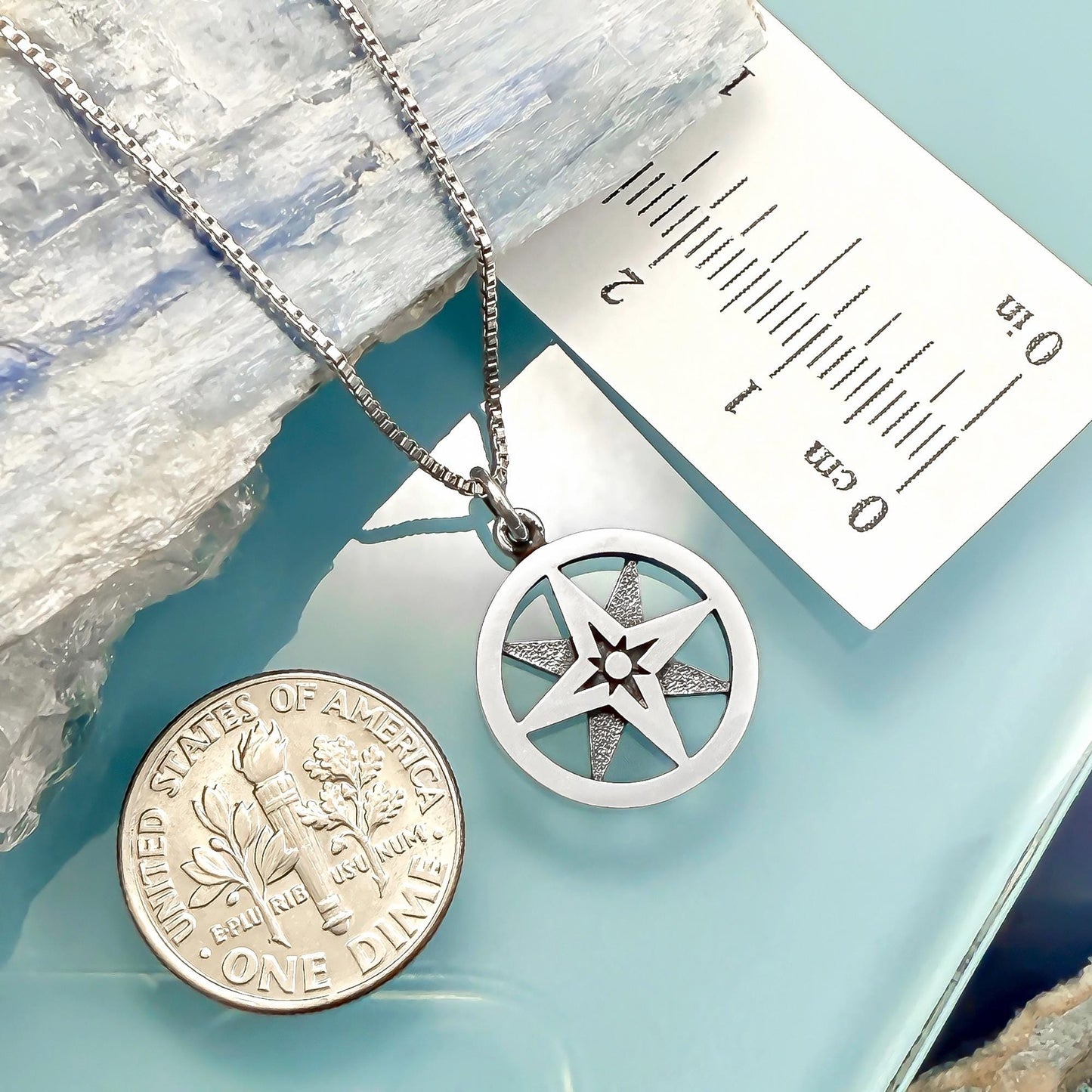 a silver necklace with a compass pendant and a United States one-dollar coin placed on a blue surface.