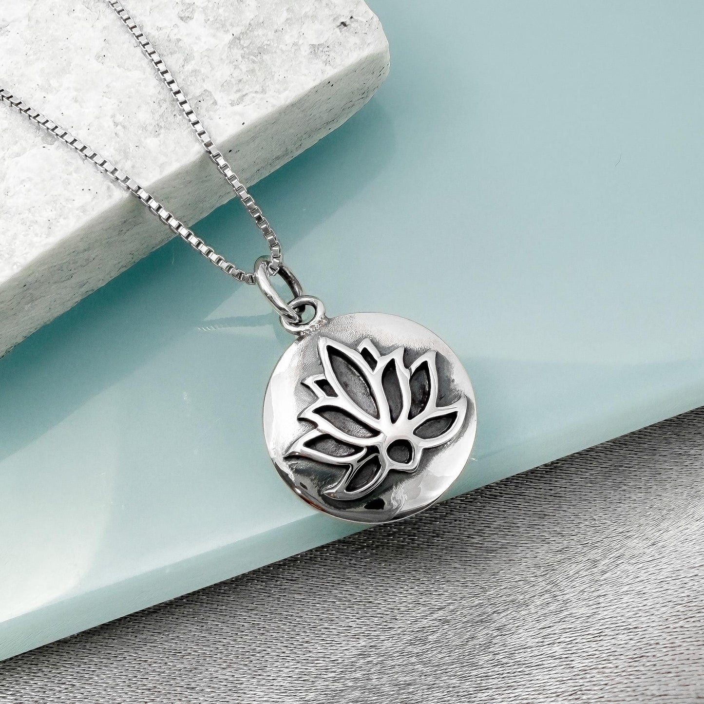 A silver-toned pendant necklace with a circular pendant featuring a lotus flower design.