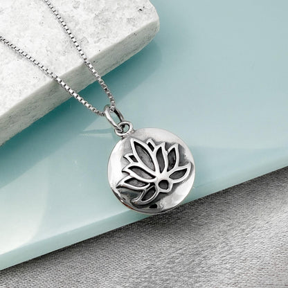 A silver-toned pendant necklace with a circular pendant featuring a lotus flower design.
