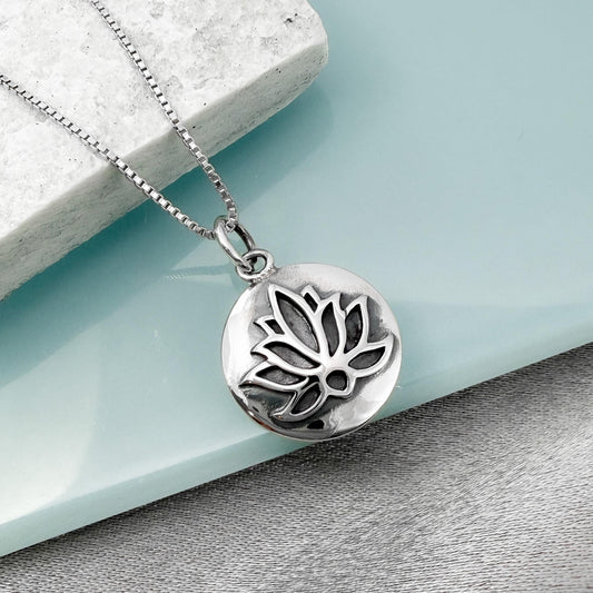 A silver-toned pendant necklace with a circular pendant featuring a lotus flower design.