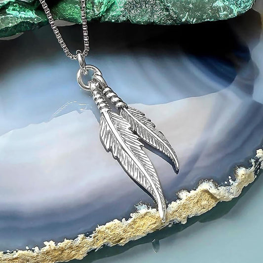 A silver pendant necklace with two feather-like pendants is displayed against a blue and green background.