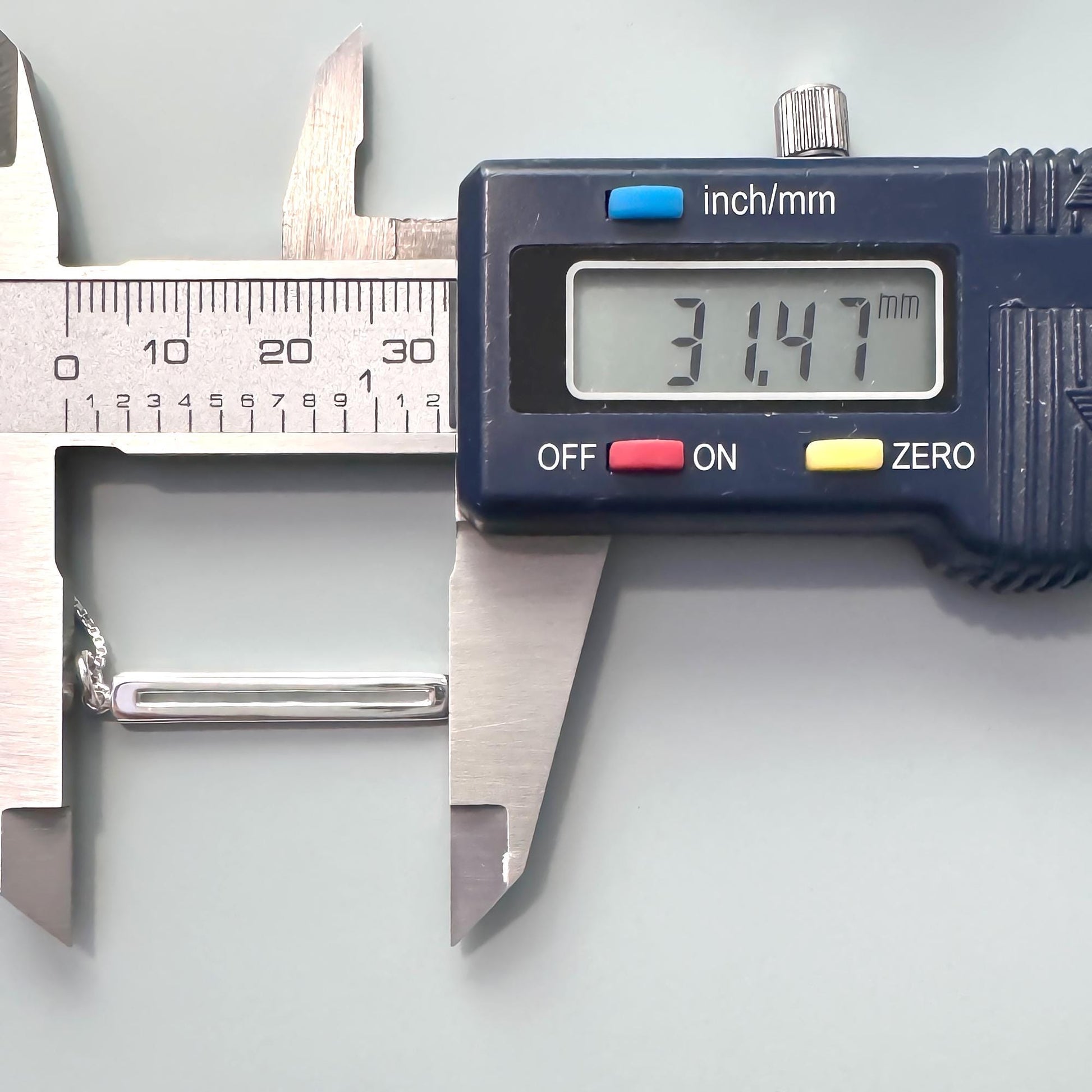 A digital caliper is being used to measure the length of a small object, which appears to be a piece of jewelry.