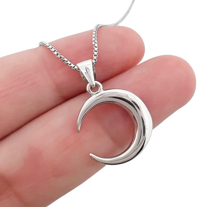 A silver crescent moon pendant is being held in a person's hand.