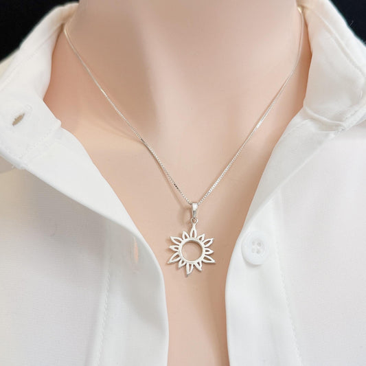 A silver necklace with a pendant featuring a sun design is shown against a white shirt collar.