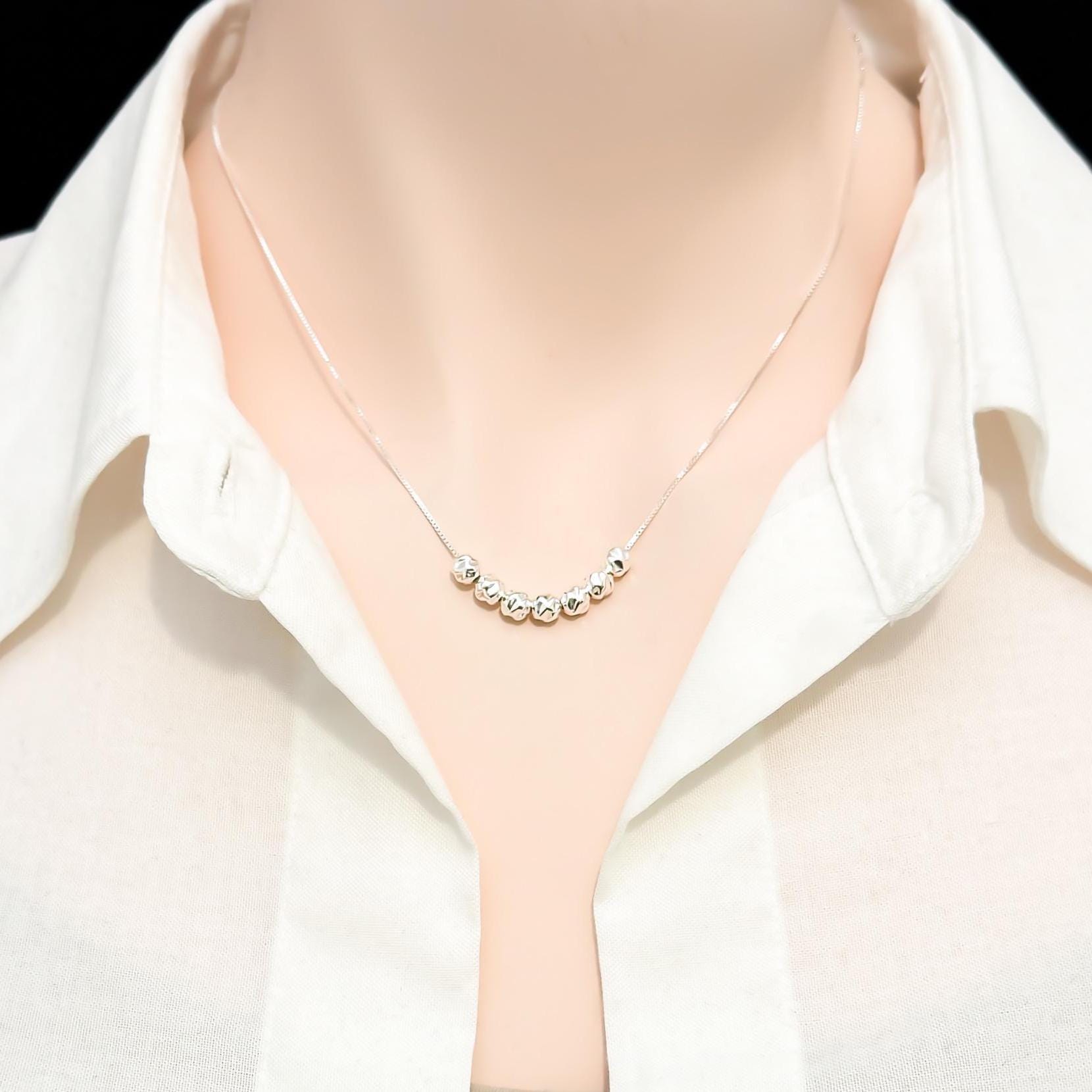 A close-up view of a person wearing a white collared shirt and a necklace with small, round beads on it.