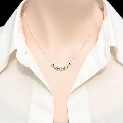 A close-up view of a person wearing a white collared shirt and a necklace with small, round beads on it.
