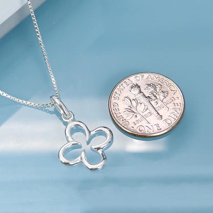 A silver flower pendant necklace and a United States one dollar coin are placed on a blue surface.