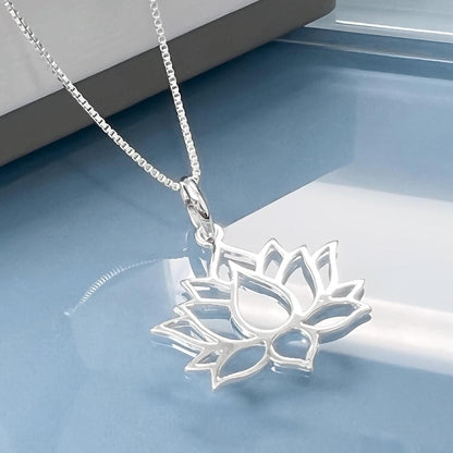 A silver necklace with a pendant in the shape of a lotus flower is displayed on a white surface.