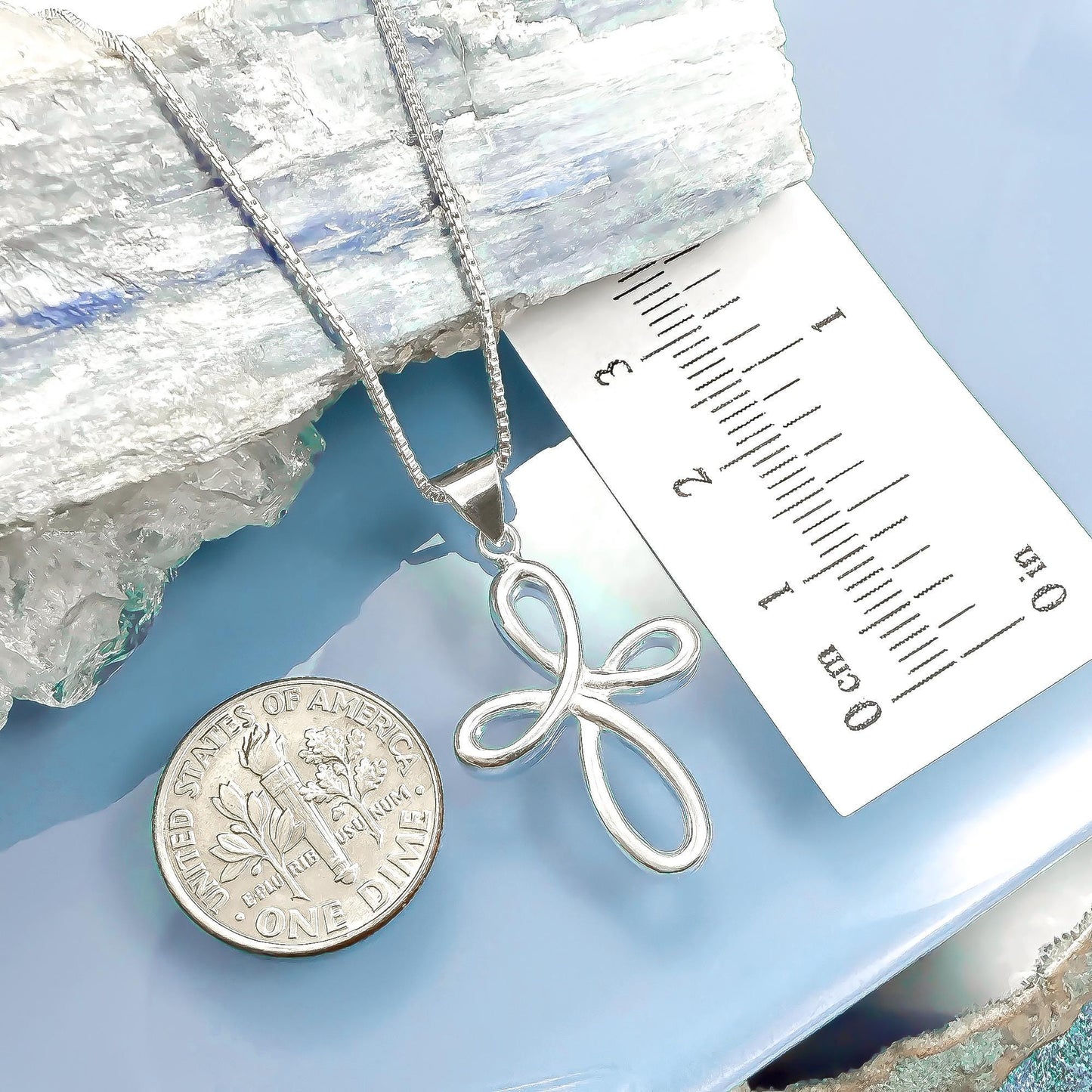 a silver cross pendant and a United States quarter coin placed on a blue surface.