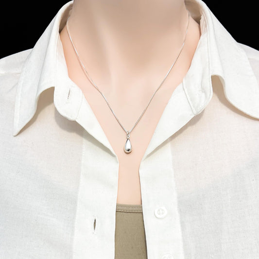 A close-up view of a person wearing a white collared shirt and a silver necklace with a pendant.