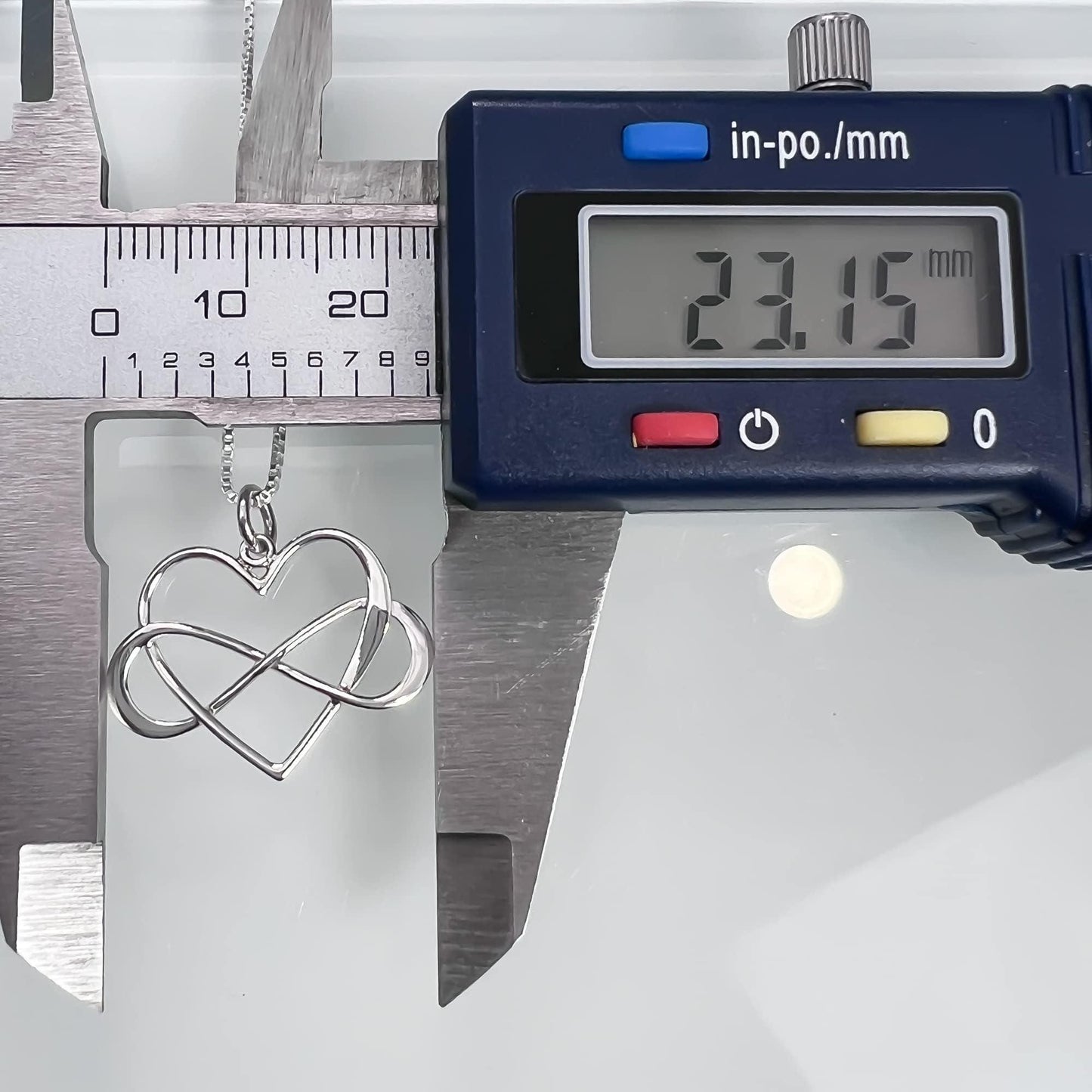 A silver heart-shaped pendant necklace is being measured with a ruler, and a digital caliper is also visible in the image.