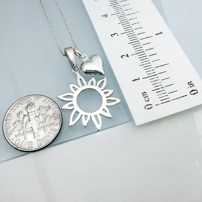 a silver necklace with a pendant and a small silver coin, along with a ruler for size comparison.