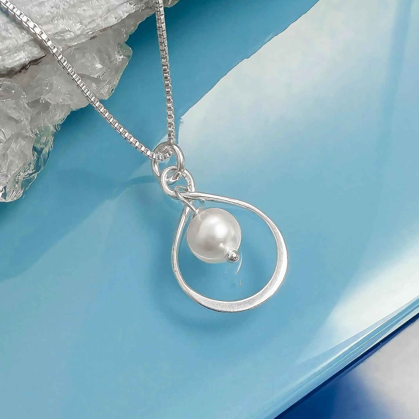 A silver necklace with a pearl pendant is displayed against a blue background.