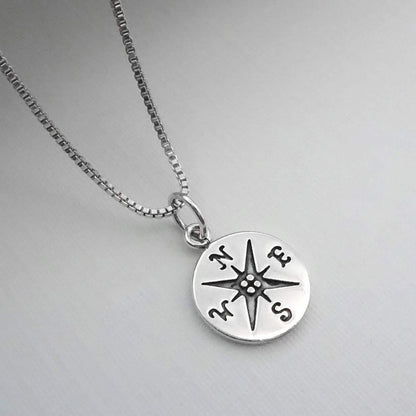 A silver-colored necklace with a compass pendant on it.