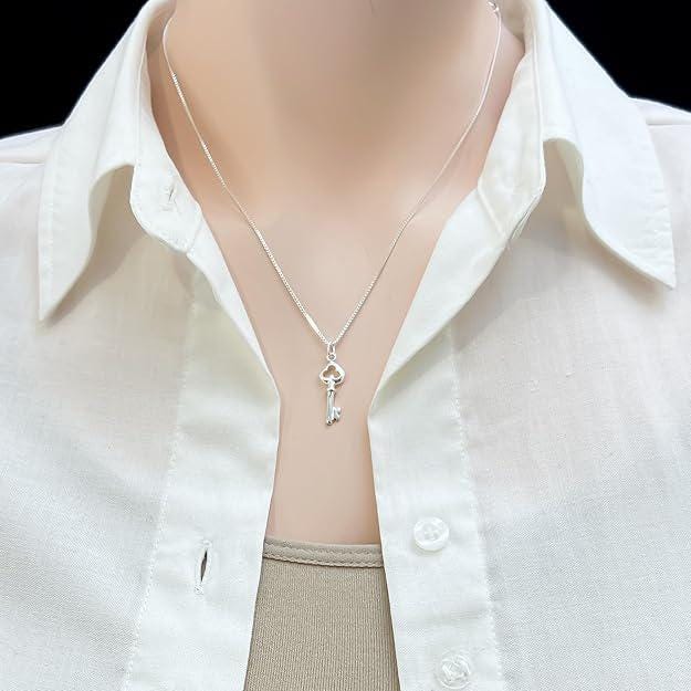 A silver necklace with a key pendant is worn around a person's neck, with a white collared shirt visible underneath.