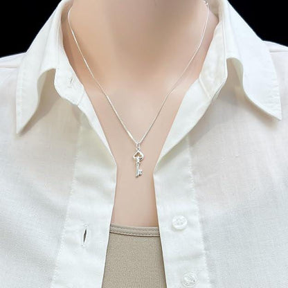 A silver necklace with a key pendant is worn around a person's neck, with a white collared shirt visible underneath.