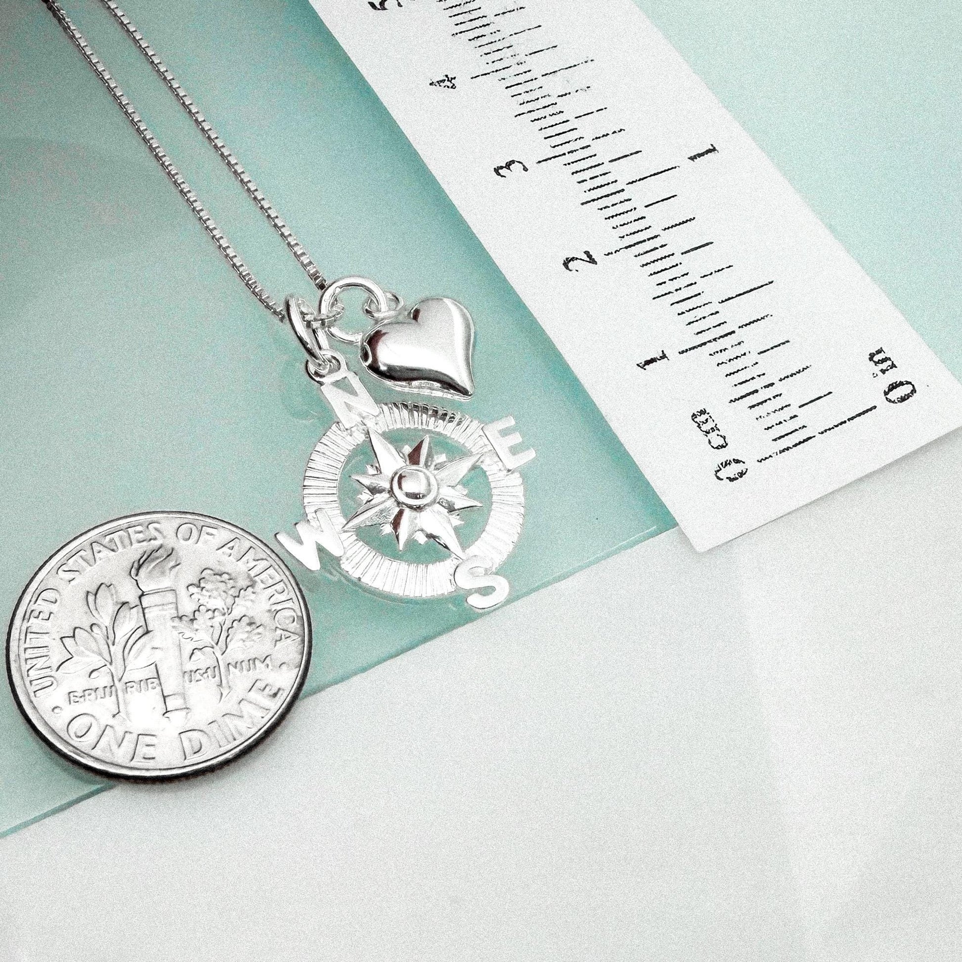 a silver compass pendant and a United States one-dollar coin, both placed on a light blue surface.
