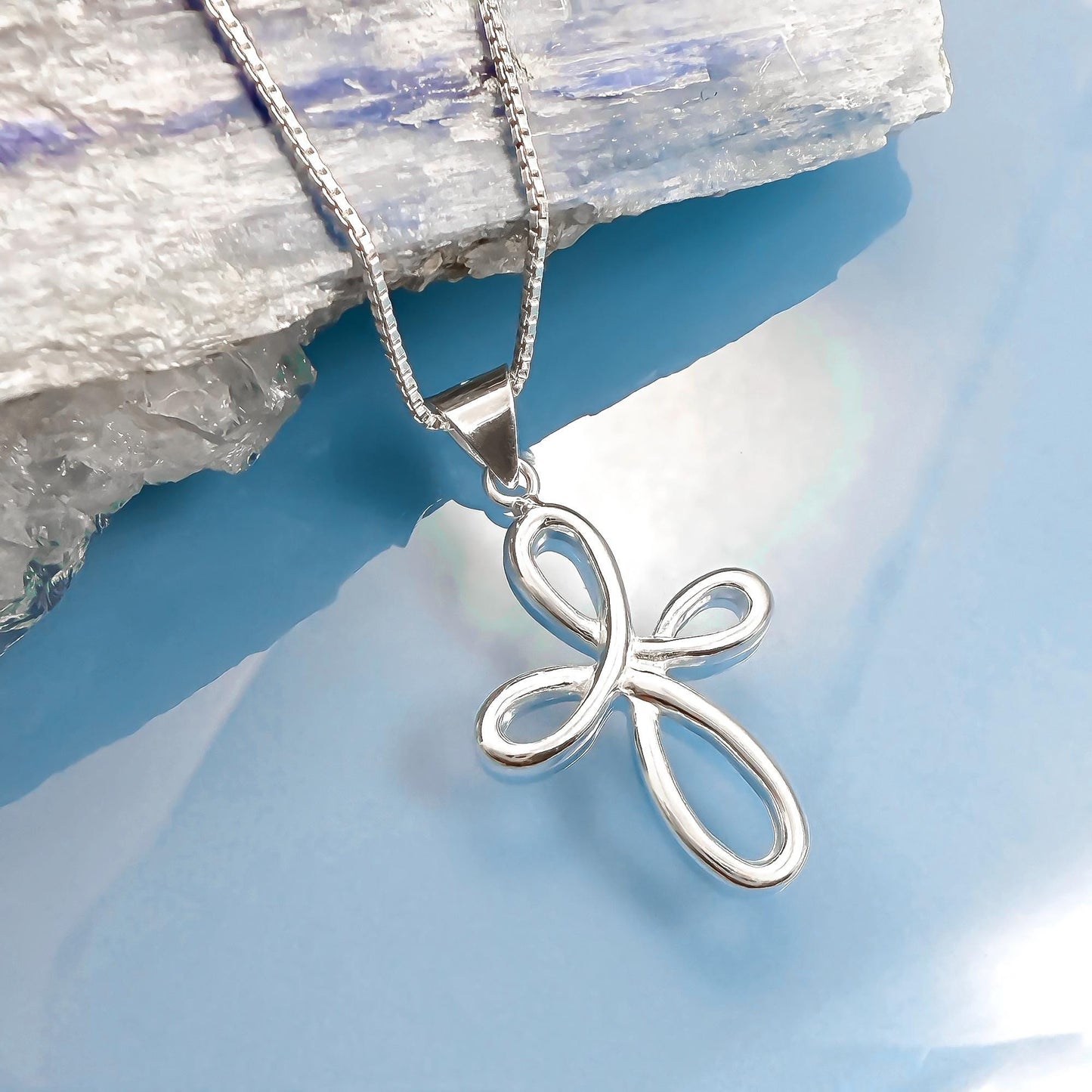 A silver cross pendant necklace is displayed against a blue background.