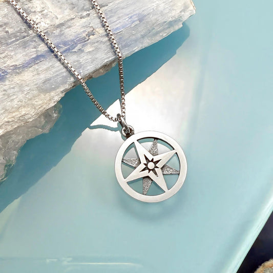 A silver necklace with a compass pendant is displayed against a blue background.