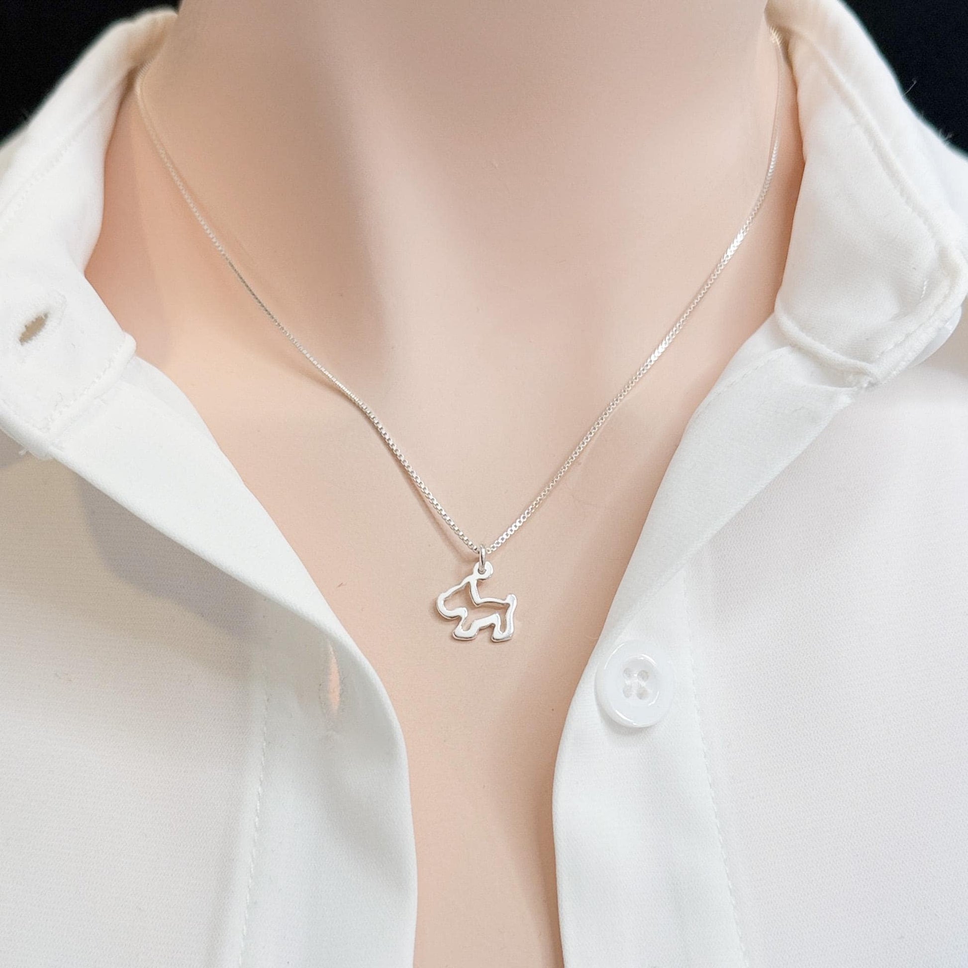 A silver necklace with a small pendant is worn around a person's neck, who is wearing a white collared shirt.