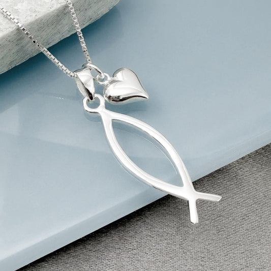 A silver necklace with a pendant featuring a fish-shaped design and a heart-shaped charm.