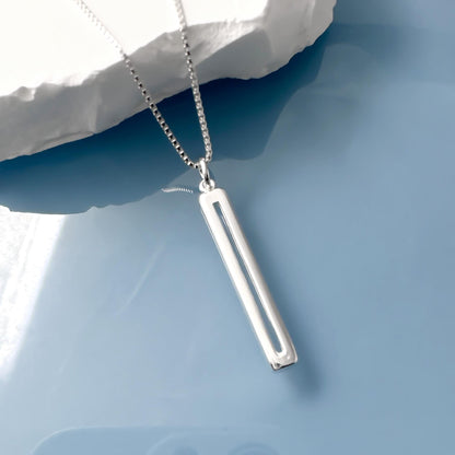 A silver necklace with a rectangular pendant is displayed against a blue background.