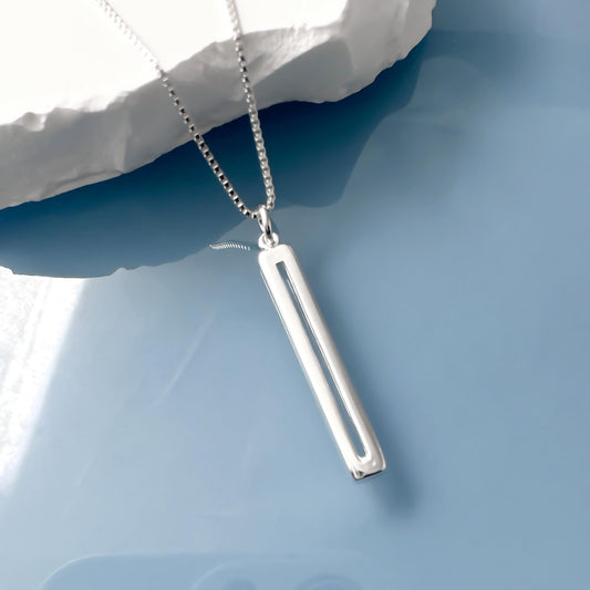 A silver necklace with a rectangular pendant is displayed against a blue background.