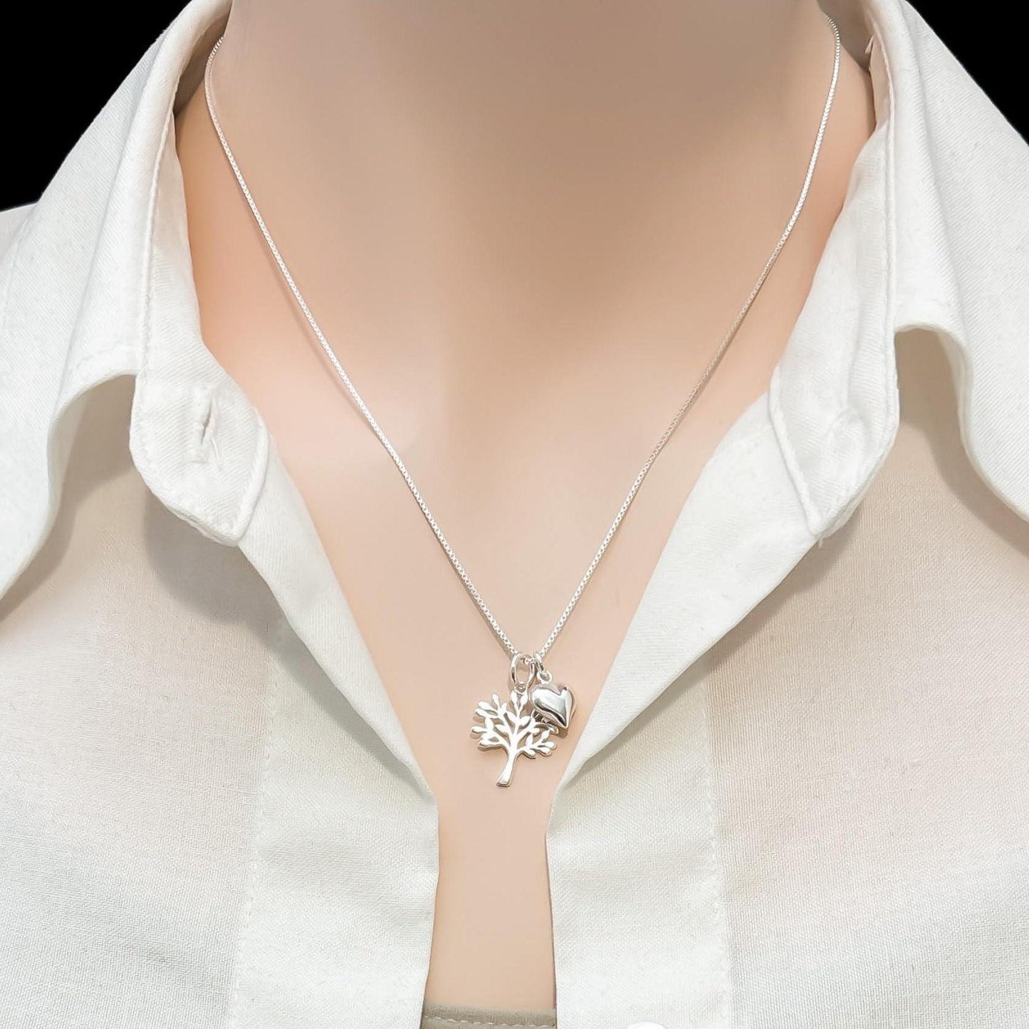 A silver necklace with a pendant is worn around a person's neck, who is wearing a white collared shirt.