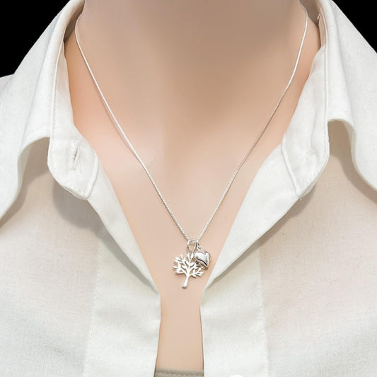 A silver necklace with a pendant is worn around a person's neck, who is wearing a white collared shirt.