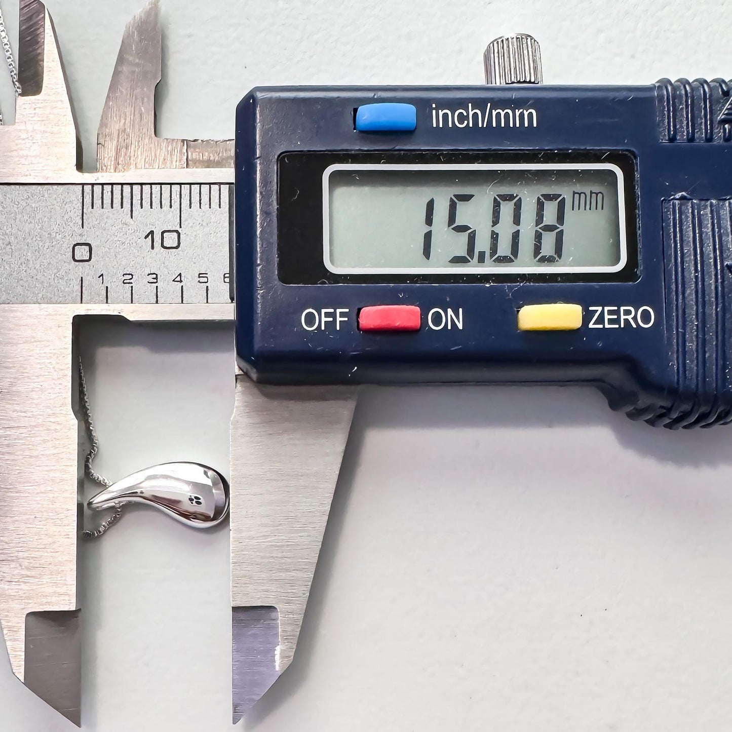 A digital caliper is being used to measure the size of a silver object, which appears to be a necklace. The caliper displays the size as 15.08 millimeters.