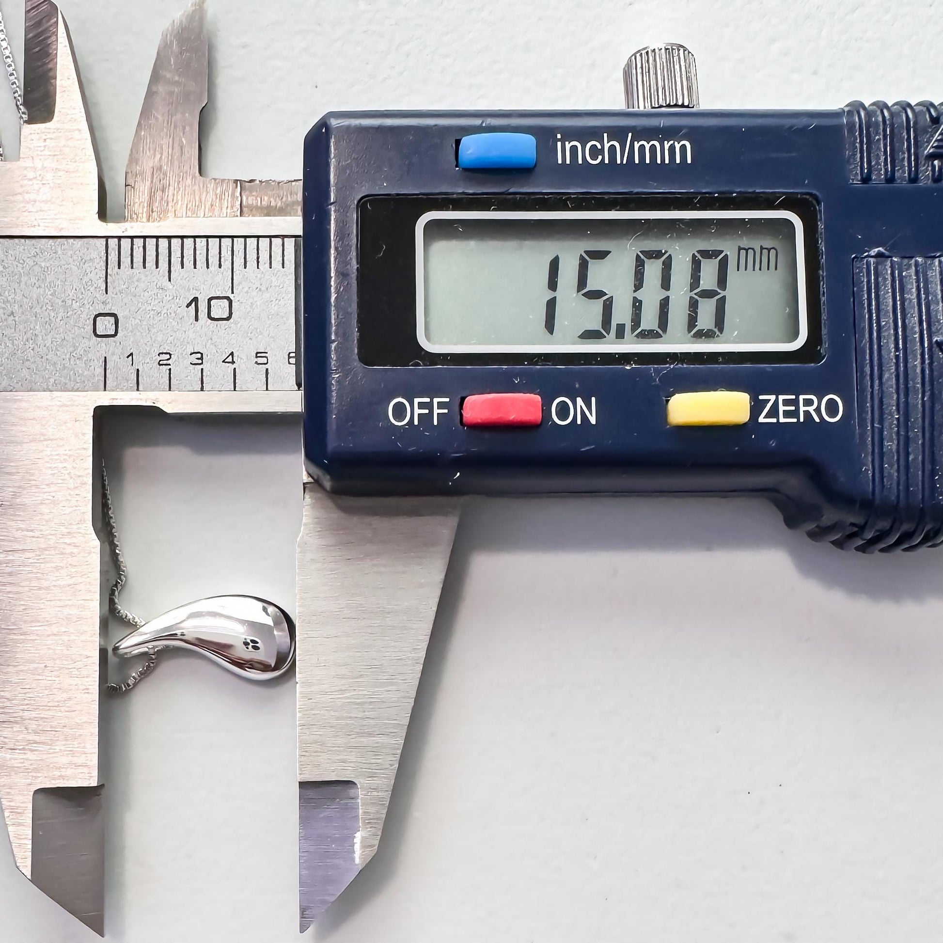 A digital caliper is being used to measure the size of a silver object, which appears to be a necklace. The caliper displays the size as 15.08 millimeters.