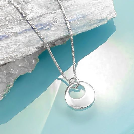 A silver necklace with a circular pendant is displayed against a blue background.