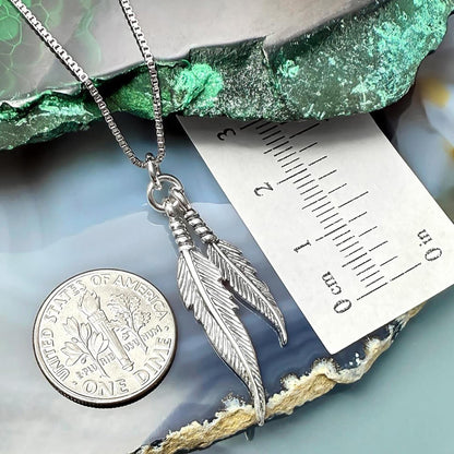 a silver feather pendant necklace with a United States quarter coin placed on top of a green rock.