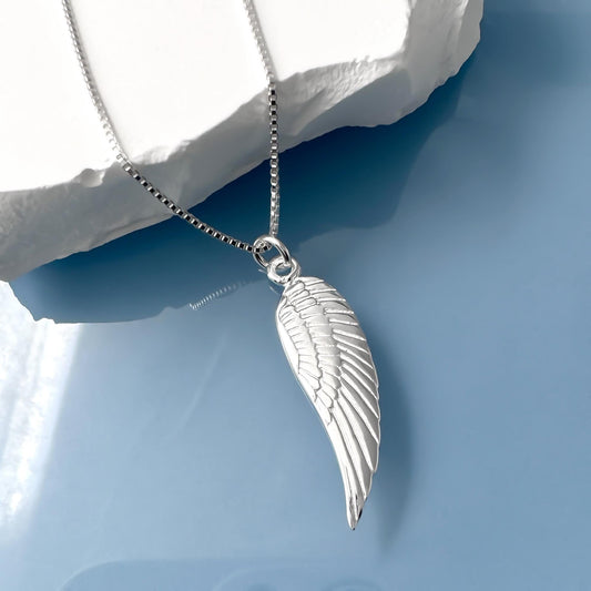 A silver necklace with a pendant featuring a winged design is displayed against a blue background.