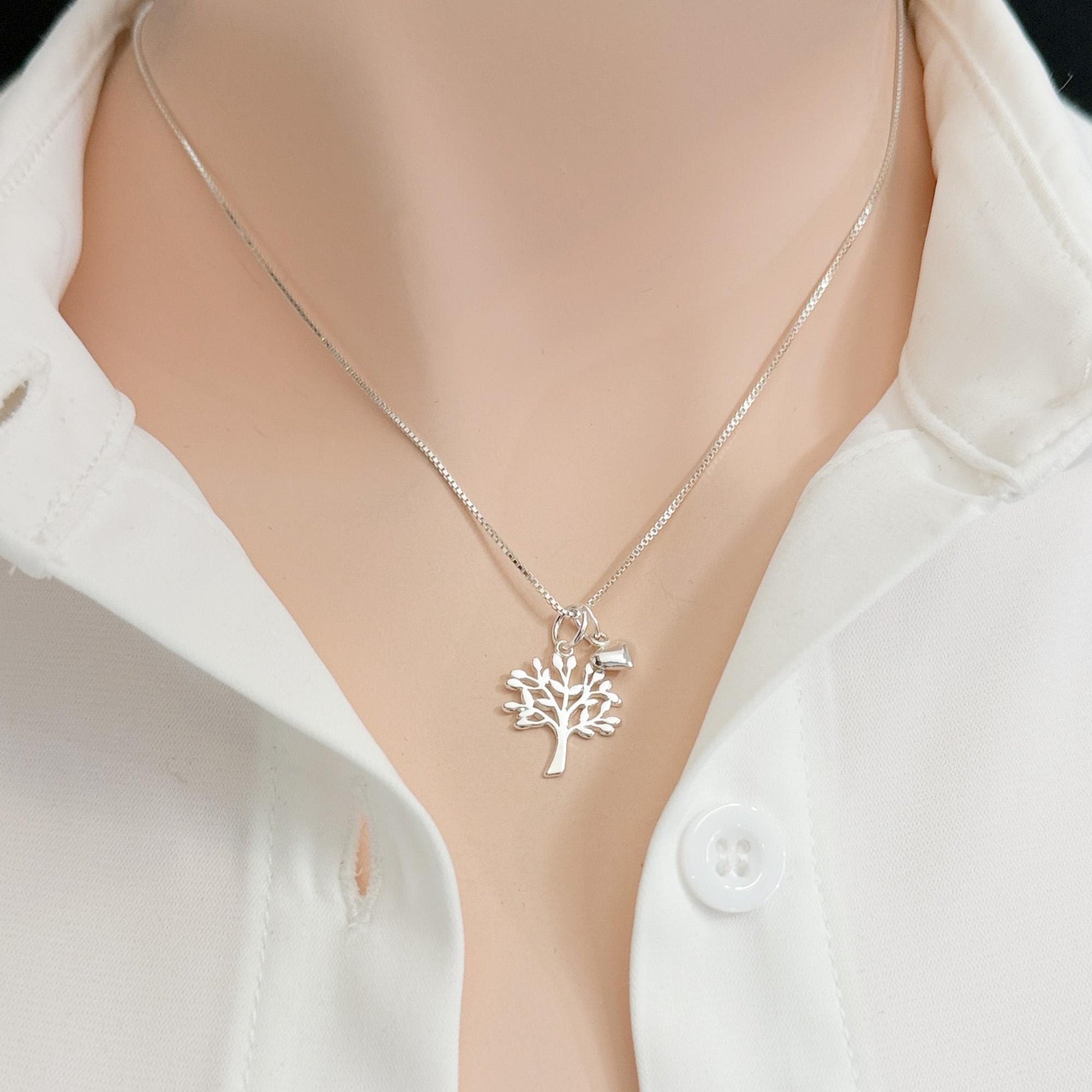 A silver necklace with a tree pendant is worn around a person's neck, and a white collared shirt is visible underneath.