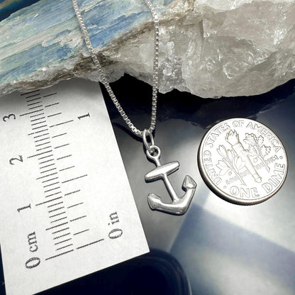 a silver anchor pendant hanging from a chain, placed next to a United States one dollar coin.