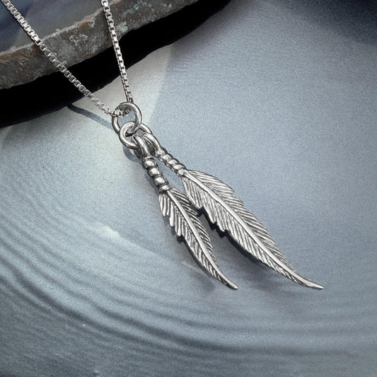 A silver-toned pendant necklace with two feather-like charms hanging from a chain.